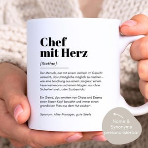 May include: White ceramic mug with a black design that reads "Chef mit Herz [Steffan]" and a definition of the term in German. The mug has a black handle and a black rim. The text on the mug is "Der Mensch, der mit einem L&auml;cheln im Gesicht versucht, das Unm&ouml;gliche m&ouml;glich zu machen - wie eine Mischung aus einem Jongleur, einem Feuerwehrmann und einem Magier, nur ohne Sicherheitsnetz oder Zauberstab. Ein Genie, das inmitten von Chaos und Drama einen klaren Kopf bewahrt und immer einen grandiosen Plan aus dem Hut zaubert. Synonym: Alles-Manager, gute Seele". The text "Name & Synonyme personalisierbar" is also on the mug.