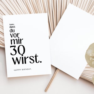 May include: A white card with black text that reads "Danke, dass du vor mir 30 wirst. HAPPY BIRTHDAY." The card is on a light brown background.