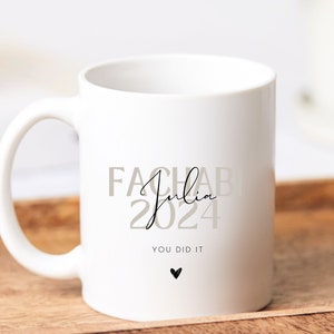 Peut inclure: Mug en céramique blanche avec du texte noir qui dit "FachAb Julia 2024 You Did It" avec un petit cœur noir.