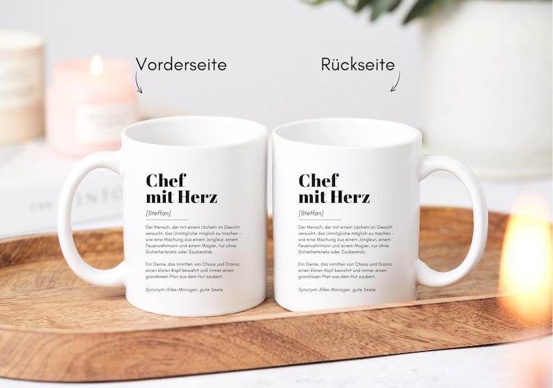 May include: Two white ceramic mugs with black text that reads "Chef mit Herz [Steffan]"  The text defines the word "Chef mit Herz" as "The person who tries their best to make the impossible possible, a leader who inspires, a person who always has a plan and never gives up."