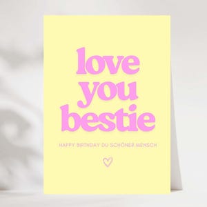 Könnte beinhalten: Eine hellgelbe Grußkarte mit den Worten "love you bestie" in pinkfarbenen, fetten Buchstaben. Darunter steht in kleineren pinkfarbenen Buchstaben "Happy Birthday Du Schöner Mensch" mit einem kleinen Herzsymbol.