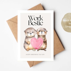 Op de afbeelding: Een wenskaart met twee aquarelotters die een roze hart vasthouden. De tekst "Work Bestie" staat boven de otters en "Happy Birthday to You" eronder. De kaart ligt op een bruine envelop.