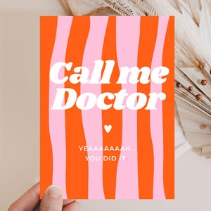 May include: A greeting card with a vibrant design. The card features a bold orange background with vertical pink wavy stripes. White text reads "Call me Doctor" with a small heart. Below, it says "YEAAAAAAH... YOU DID IT".