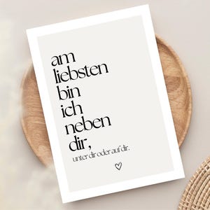 May include: A framed print with the text "am liebsten bin ich neben dir, unter dir oder auf dir." in black, with a heart symbol. The print is on a light beige background and is displayed on a wooden plate.