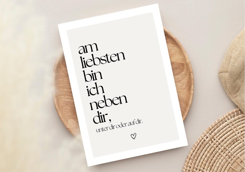 May include: A framed print with the text "am liebsten bin ich neben dir, unter dir oder auf dir." in black, with a heart symbol. The print is on a light beige background and is displayed on a wooden plate.