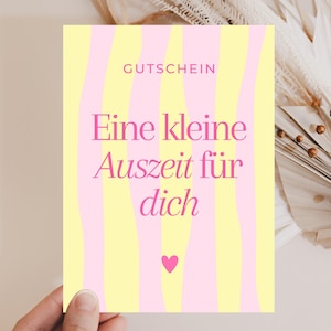 May include: A gift voucher with a yellow and pink striped design. The word "GUTSCHEIN" is at the top, with the text "Eine kleine Auszeit für dich" in pink script below. A small pink heart is at the bottom.