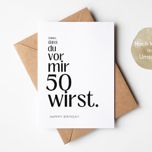May include: A white card with black text that reads "Danke, dass du vor mir 50 wirst."  The text "HAPPY BIRTHDAY." is below the main text. The card is sitting on a brown envelope with the text "Nach Wunsch inkl. Umschlag" on the envelope.