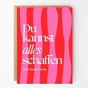 Könnte beinhalten: Eine Grußkarte mit einem wellenförmigen Streifendesign in Rot und Pink. Die Karte zeigt den deutschen Text "Du kannst alles schaffen" in Weiß, mit dem Satz "Denk immer daran" darunter. Die Karte befindet sich in einem braunen Umschlag.