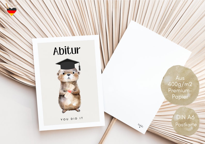 May include: A graduation card featuring a cartoon otter wearing a graduation cap and holding a diploma. The card is beige with black text that reads "Abitur" and "You Did It". The card is printed on 400g/m2 premium paper and is a DIN A6 postcard.