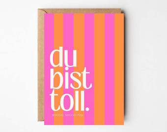 May include: Greeting card with a vertical striped pattern in pink and orange. The card features the German phrase "du bist toll" in white, along with the words "sooooo, sooooo toll" at the bottom. The card is inside a brown envelope.