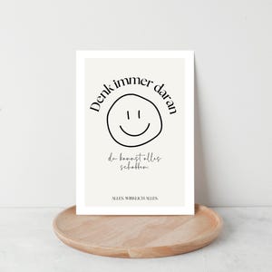 May include: A framed print with a cream background and black text. The text includes the phrase "Denk immer daran" above a smiley face, and "da kannst alles schaffen" below. The print is on a wooden tray.