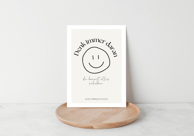 May include: A framed print with a cream background and black text. The text includes the phrase "Denk immer daran" above a smiley face, and "da kannst alles schaffen" below. The print is on a wooden tray.