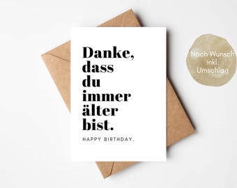 Könnte beinhalten: Eine weiße Geburtstagskarte mit schwarzem Text: "Danke, dass du immer älter bist. HAPPY BIRTHDAY." Die Karte liegt auf einem braunen Umschlag. Ein kleiner, runder, beiger Aufkleber mit deutschem Text befindet sich oben rechts.