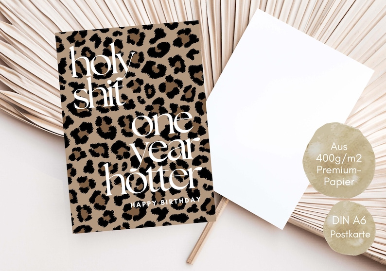 Puede incluir: Una tarjeta de cumplea&ntilde;os rectangular con un estampado de leopardo en marr&oacute;n y negro y texto en blanco que dice holy shit one year hotter HAPPY BIRTHDAY. La tarjeta incluye un sobre blanco en blanco y dos etiquetas circulares beige.