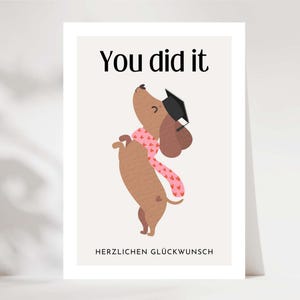 Peut inclure: Carte de félicitations de fin d'études avec un teckel de dessin animé portant une toque et une écharpe rose à motifs de cœurs. Le texte "You did it" est en haut, avec "HERZLICHEN GLÜCKWUNSCH" en bas.