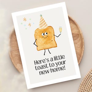 May include: A greeting card featuring a cartoon toast character wearing a party hat and holding a champagne glass. The card has the text "Here's a little toast to your new home!" on a white background.