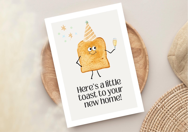 May include: A greeting card featuring a cartoon toast character wearing a party hat and holding a champagne glass. The card has the text "Here's a little toast to your new home!" on a white background.