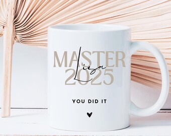 Könnte beinhalten: Weiße Keramiktasse mit dem Text "Master 2025" in brauner Schrift und "You Did It" in schwarzer Schrift. Ein kleines Herz befindet sich unter dem Text.
