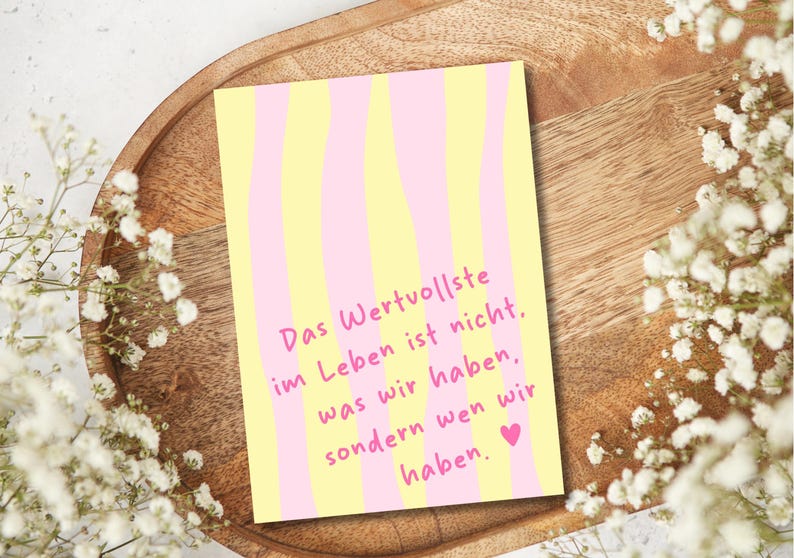 May include: A greeting card with a yellow and pink striped design. The card features the German text "Das Wertvollste im Leben ist nicht, was wir haben, sondern wen wir haben." A small pink heart is at the bottom.
