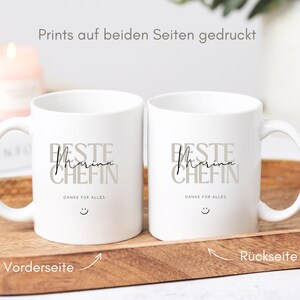 May include: Two white ceramic mugs with black text that reads "Beste Marina Chefin" and "Danke f&uuml;r alles" with a smiley face. The mugs are printed on both sides.