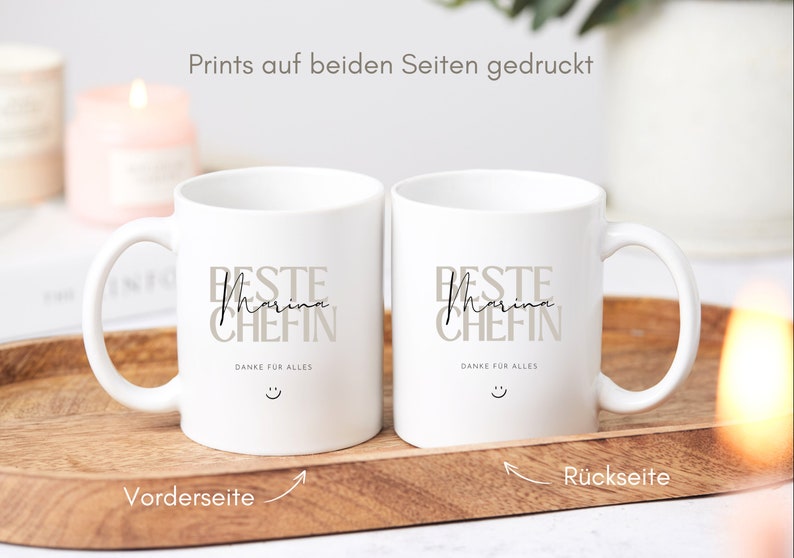 May include: Two white ceramic mugs with black text that reads "Beste Marina Chefin" and "Danke f&uuml;r alles" with a smiley face. The mugs are printed on both sides.