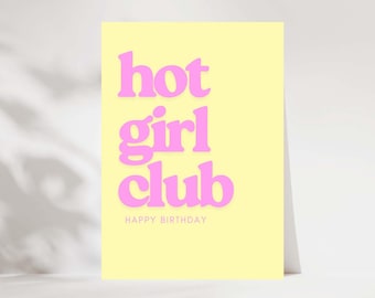 May include: A greeting card with a light yellow background and the words "hot girl club" in large, pink, bubble letters. Below, in smaller text, it reads "HAPPY BIRTHDAY". The card is leaning against a white surface.