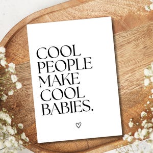 Pu&ograve; includere: Un biglietto bianco con testo nero che recita "COOL PEOPLE MAKE COOL BABIES." Un piccolo cuore &egrave; disegnato nella parte inferiore del biglietto.