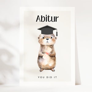 May include: A graduation card featuring a cartoon otter wearing a black graduation cap and holding a diploma. The card has the text "Abitur" and "You Did It" on it.