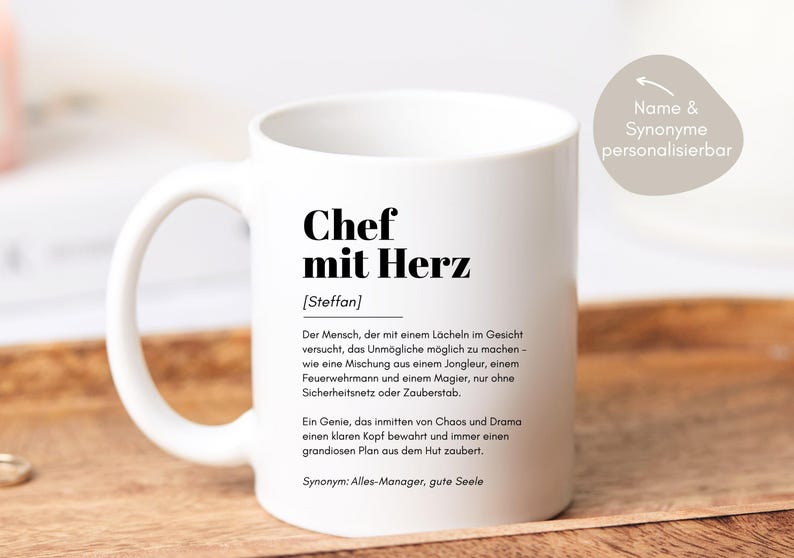 May include: White ceramic mug with black text that reads "Chef mit Herz [Steffan]" and a definition of the term in German. The text says "The person who tries to make the impossible possible with a smile on their face - like a mix of a juggler, a firefighter and a magician, only without a safety net or magic wand. A genius who keeps a clear head in the midst of chaos and drama and always conjures up a grand plan out of their hat. Synonym: All-Manager, good soul."
