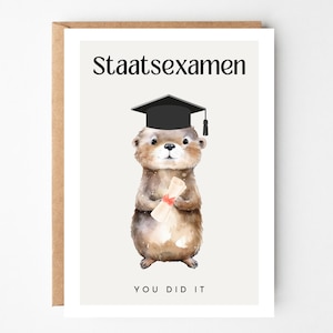 Könnte beinhalten: Eine Grußkarte mit einer Aquarellillustration eines braunen Otters, der eine schwarze Doktorhut trägt und ein mit einem roten Band gebundenes Diplom hält. Der Text Staatsexamen steht über dem Otter und YOU DID IT steht darunter.
