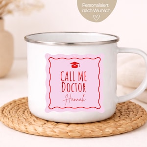 Könnte beinhalten: Weißer Emaille-Becher mit silbernem Rand, mit einem rosa Quadrat mit rotem Rahmen. Das Quadrat hat ein Abschlusskappen-Symbol und die Worte "CALL ME DOCTOR Hannah" in Rot. Der Becher steht auf einem gewebten Untersetzer.