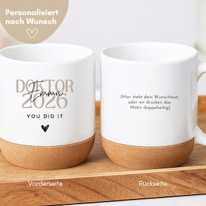 Könnte beinhalten: Zwei weiße Keramikbecher mit Korkboden. Der linke Becher zeigt den Text DOKTOR Emma 2026 YOU DID IT mit einem kleinen Herzsymbol. Der rechte Becher trägt den Text (Hier steht dein Wunschtext, oder wir drucken das Motiv doppelseitig).