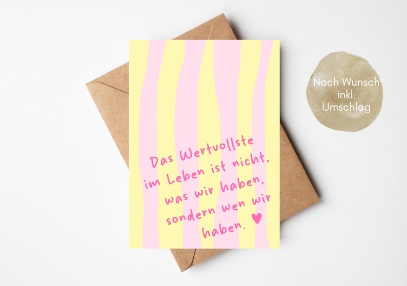 May include: A greeting card with a yellow and pink striped design. The card has the German text "Das Wertvollste im Leben ist nicht, was wir haben, sondern wen wir haben." A brown envelope is behind the card.