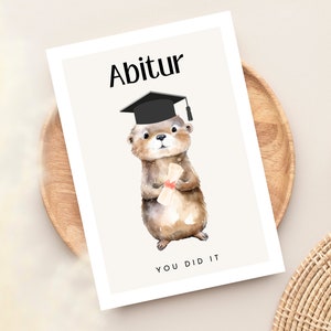 May include: A graduation card featuring a cute otter wearing a black graduation cap and holding a diploma. The card has the text "Abitur" and "You Did It" on it.