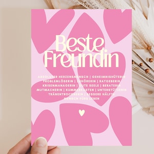 Könnte beinhalten: Eine rechteckige Karte mit hellrosa Hintergrund und mehreren dunkelrosa Herzformen. Der Text "Beste Freundin" ist in großen cremefarbenen Buchstaben gedruckt, gefolgt von einer Liste deutscher Begriffe wie "Herzensmensch" und "Zuhörerin".