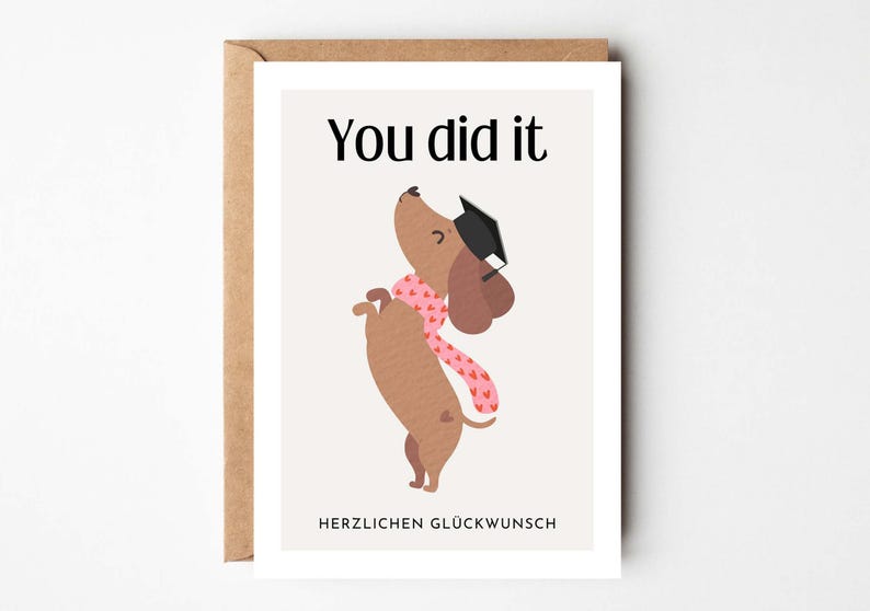 May include: A graduation greeting card featuring a dachshund wearing a graduation cap and a pink scarf with hearts. The card reads "You did it" at the top and "HERZLICHEN GL&Uuml;CKWUNSCH" at the bottom. The card is in a brown envelope.