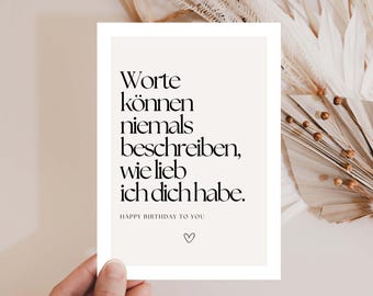 May include: A greeting card with the text "Worte können niemals beschreiben, wie lieb ich dich habe. HAPPY BIRTHDAY TO YOU" in black font. The card is held by a hand and has a heart symbol at the bottom.