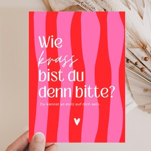 May include: A rectangular greeting card featuring a vertical wavy striped pattern in alternating shades of bright pink and red. The card displays the white text "Wie krass bist du denn bitte?" followed by "Du kannst so stolz auf dich sein." and a small white heart icon.