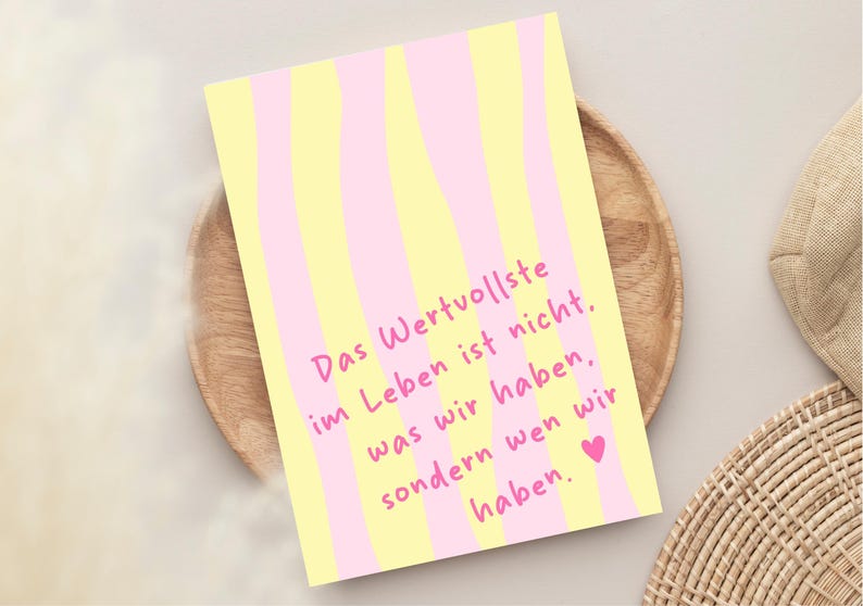 May include: A greeting card with a yellow and pink striped pattern. The card features the German text "Das Wertvollste im Leben ist nicht, was wir haben, sondern wen wir haben" in pink, with a pink heart at the bottom.