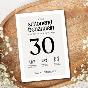 May include: A white card with black text that reads "ACHTUNG, schonend behandeln DAS GUTE ST&Uuml;CK IST SCHON 30" and has three laundry care symbols below the number 30. The symbols indicate that the item should be hand washed, not ironed, and not machine dried. The card also says "HAPPY BIRTHDAY" at the bottom.