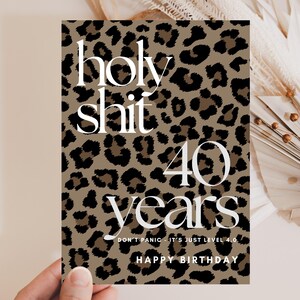 Könnte beinhalten: Eine rechteckige Geburtstagskarte mit einem braun-schwarzen Leopardenmuster. Der Text lautet holy shit 40 years, DON'T PANIC - IT'S JUST LEVEL 4.0 und HAPPY BIRTHDAY in einer weißen Serifenschrift, die mittig auf der Karte platziert ist.