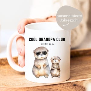 Peut inclure: Mug en céramique blanche avec une illustration en noir et blanc de deux loutres. La tasse indique "Cool Grandpa Club Since 2024".