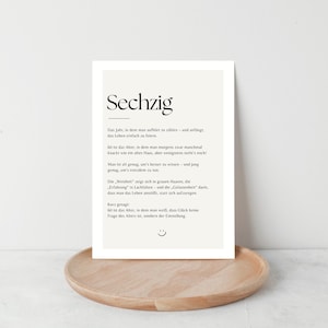 May include: A framed print with the German word "Sechzig" at the top, meaning sixty. The print has a cream-colored background with black text. It is displayed on a round, light brown wooden tray.