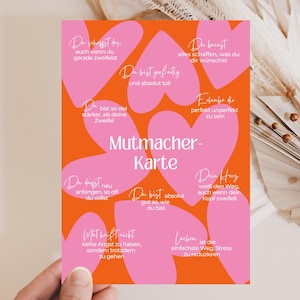 Könnte beinhalten: Eine rechteckige Karte mit orangefarbenem Hintergrund und mehreren rosa Herzformen. Der Text lautet Mutmacher-Karte, ergänzt durch verschiedene deutsche Sätze wie Du schaffst das, Du bist großartig und Erlaube dir perfekt unperfekt zu sein.