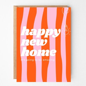 Peut inclure: Carte de vœux avec une enveloppe marron. Le recto présente un fond orange vif avec des rayures roses ondulées. Le texte blanc indique "happy new home" et "It's going to be amazing". Une illustration d'ampoule est en haut à droite.