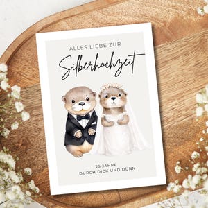 May include: A rectangular greeting card featuring a watercolor illustration of two otters dressed as a bride and groom. The text reads ALLES LIEBE ZUR Silberhochzeit and 25 JAHRE DURCH DICK UND D&Uuml;NN. The background is a light cream color.
