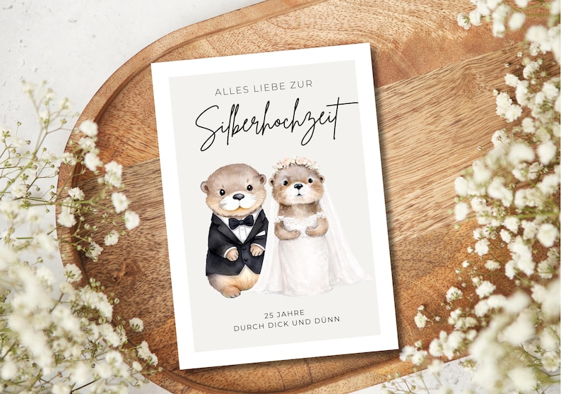 May include: A rectangular greeting card featuring a watercolor illustration of two otters dressed as a bride and groom. The text reads ALLES LIEBE ZUR Silberhochzeit and 25 JAHRE DURCH DICK UND D&Uuml;NN. The background is a light cream color.