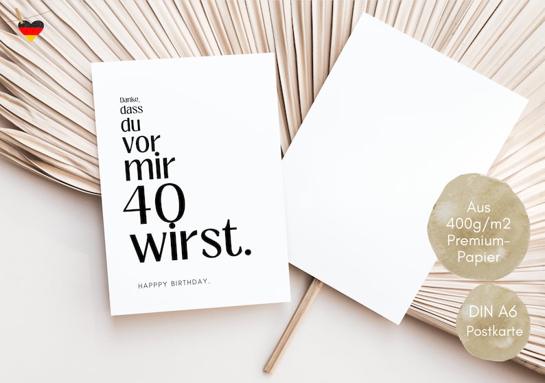 May include: A white card with black text that reads "Danke, dass du vor mir 40 wirst. HAPPY BIRTHDAY." The card is sitting on a light brown background.