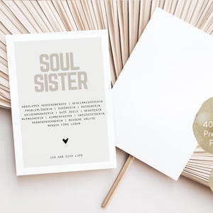 May include: A light brown postcard with the text "SOUL SISTER" in black lettering. The text below reads "ABSOLUTER HERZENEMENSCH | GEHEIMNISH&Uuml;TERIN | PROBLEMLOBERIN | ZUMORERIN | MATUERERIN | KRISENMANAGERIN | GUTE SEELE | BERATERIN | NUTRACHERIA | KOMNERKASTEN | UNTERST&Uuml;TZERIN | TRANENTROCKNERIN | BESSERE H&Auml;LFTE | MENSCH F&Uuml;RS LEBEN". The text at the bottom reads "ICH HAB DICH LIEB". The postcard is made of 400g/m2 premium paper and is DIN A6 size.