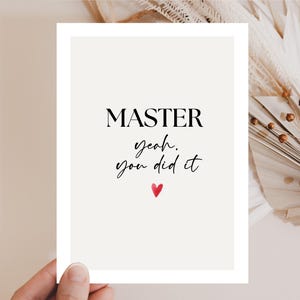 Könnte beinhalten: Eine weiße Karte mit den Worten "MASTER yeah, you did it" in schwarzer Schrift und einem kleinen roten Herz. Die Karte wird von einer Hand gehalten, mit getrockneten Blumen im Hintergrund.